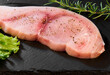 Raw Swordfish fillet covered with black pepper and with rosemary sprigs on black slate plate.