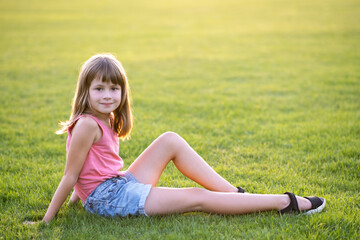 Wall Mural - Young pretty child girl laying down on green grass lawn on warm summer day.