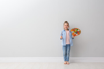 Sticker - Little girl with brush and paint palette near light grey wall indoors. Space for text