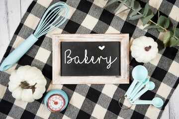 Kitchen wooden sign chalkboard mockup. On-trend farmhouse aesthetic flatlay svg craft product mock up with black plaid table cloth and white pumpkins on a white wood background. Negative copy space.