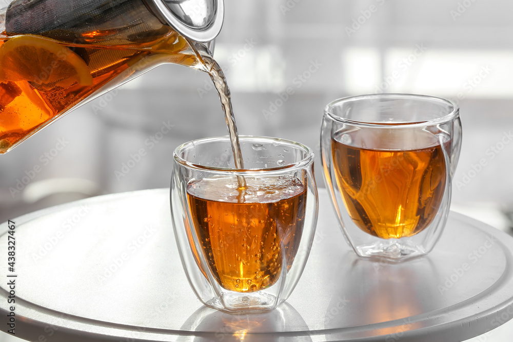 Pouring hot beverage from teapot into glasses in room, closeup