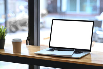 Wall Mural - Mock up laptop, notebook and coffee cup on wooden table near window.