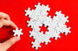 © Hasim Ramle - a hand fixing white jigsaw puzzle resemble incomplete heart love icon logo sign symbol in plain red background. selective focus