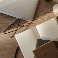 Wall Mural - Flatlay of laptop, notebook, glasses on wooden background. Home office workspace in sunlight shadows. Flat lay, top view aesthetic blog, web, social media composition.
