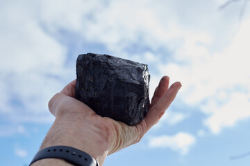 A man in his hand holds a coal against the blue sky, pollution of nature.