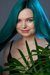 © Anna - Girl with blue green hair on a gray background, blue backlighting. Tropical plants around. Bright colored appearance of a creative person