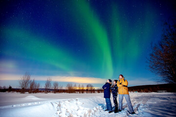 company of friends tourist looks aurora northern lights night at forest, soft focus