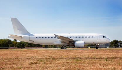 A white plane on the airport runway is taxiing. Takeoff and landing. Arrival and departure. Place for text. Passenger plane mockup. Airplane flight. Travel by air transport. Copy space