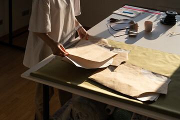Fashion designer hold new sewing patterns on craft paper, unrecognizable closeup. Female tailor work with clothes models drafting in studio. Seamstress in atelier workshop. Tailoring business concept