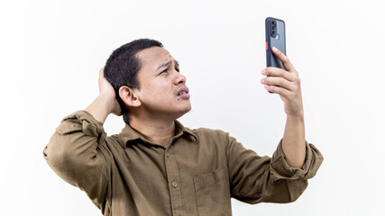 Struggling face expression of young Asian Malay man searching for coverage on the smartphone on isolated white background. Man stressed out to get the internet and phone line network.