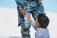 Ethnic Boy Drinking Water Near Soldier