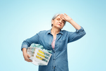 Poster - cleaning, wash and old people concept - tired senior woman in denim shirt with laundry basket over blue background