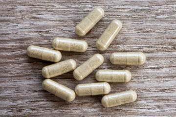 Green natural herbal medicine capsule pills isolated on wood 