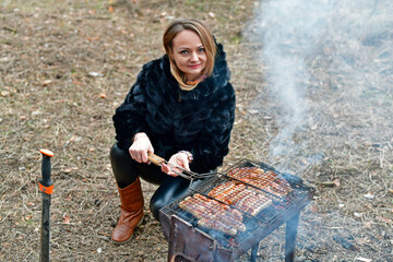 Beautiful woman fries sausages on the grill, early spring.