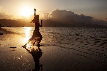 Wall Mural - Beautiful woman dancing by the sea at sunset