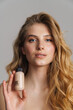 © Drobot Dean - Half-naked blonde woman looking at camera while showing cosmetic product
