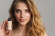 © Drobot Dean - Half-naked blonde woman looking at camera while showing cosmetic product