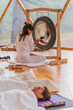 © ADDICTIVE STOCK - Spiritual woman hitting gong while calm people lying on yoga mats with eyes closed in yoga class