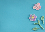 Fototapeta Storczyk - On a blue background is a composition of crocheted products. Imitation of a spring or summer day with flower or plant and butterfly. Green friday