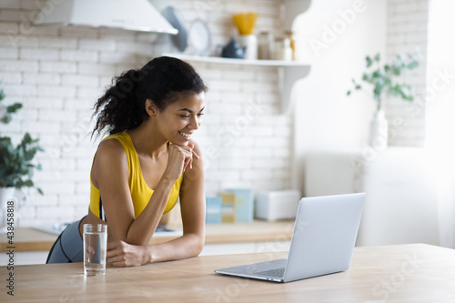 Young beautiful African American woman using laptop to watch online fitness webinar, happy smiling female gets a virtual consultation about healthy eating and lifestyle, video call