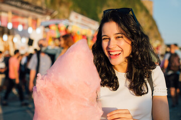 Wall Mural - Happy young laughing woman eating cotton candy at fairground