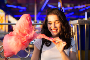 Wall Mural - Happy young woman eating cotton candy at fairground