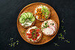 Four crispy buckwheat bread with cream cheese, radish, tomato, chickpea, cucumber and microgreen for healthy breakfast on parchment paper on black stone background. Concept vegan and healthy eating.