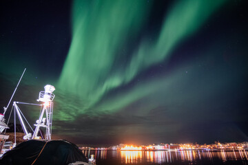 Wall Mural - Aurora borealis, Northern lights over illuminated Reine town on coastline at Lofoten Islands