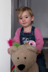 Wall Mural - Vertical selective focus portrait of adorable fair toddler girl sitting on bear toy playing