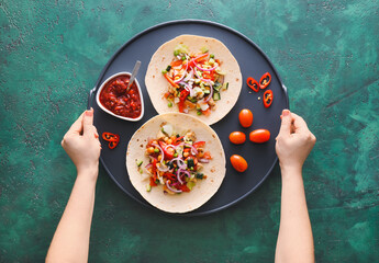 Female hands with tasty tacos and sauce on color background