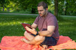 © Irene Castro Moreno - Photo of a young and attractive man sitting in the park on a towel enjoying a sunny day outside in the nature and checking his tablet. Electronic device, technology
