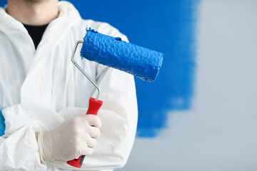 Wall Mural - Man builder repairman holding roller with blue paint in his hands closeup