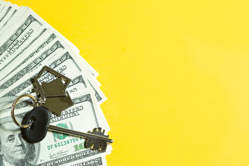 Home key with a keychain on a stack of $ 100 bills on yellow background. Purchase of an apartment, house, real estate, business, mortgage and housing loan from bank, savings, cash, moving. Copy space