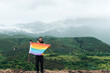 © Alberto - person holding rainbow lgbt pride flag with mountains landscape and fog background. mountain sports and social inclusion.