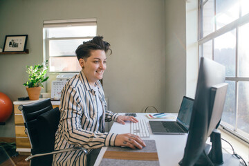 smiling woman with short hair in striped shirt working on computer in home office