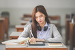 © EduLife Photos - Stock photo of a young teenage woman Asian college student in student uniform studying and writing on digital tablet in a university classroom