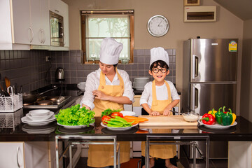 Wall Mural - Asian woman young mother with son boy cooking salad food with vegetable holding tomatoes and carrots, bell peppers on plate for happy family cook food enjoyment lifestyle kitchen in home