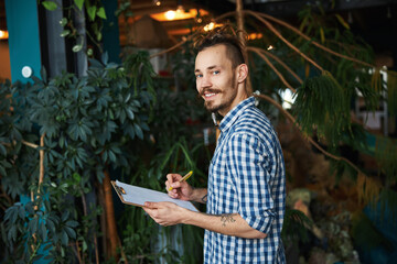 Wall Mural - Cheerful young man writing on clipboard at home