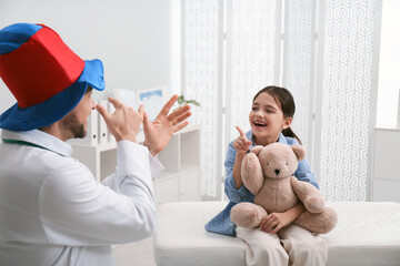 Wall Mural - Pediatrician in funny hat playing with little girl during visit at hospital