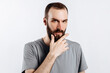 © Daria Lukoiko - Serious puzzled handsome male model with beard holding hand on chin as if thinking about something, squinting at camera with suspicious look and standing over gray background. Man decides what to buy