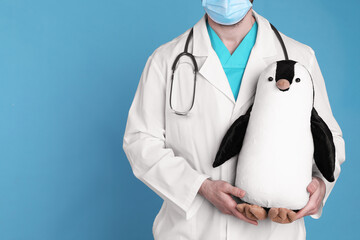 Wall Mural - Pediatrician with toy penguin and stethoscope on light blue background, closeup. Space for text