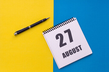 August 27th. Day of 27 month, calendar date. A notebook with a spiral and a pen lies on a yellow-blue background, flat lay, copy space