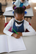 © Wavebreak Media - African american girl wearing face mask studying while sitting on her desk in the class at school