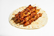 A classic Greek dish is souvlaki, small chicken kebabs. Fast food cooked on skewers and grills. Shish kebab on pita bread on a white background.