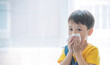 Little boy blowing nose into tissue paper and wearing surgical face mask. Copy space.