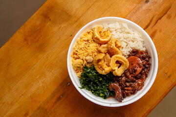 Feijoada, the Brazilian cuisine tradition.Delicious dish made of feijoada with crackling. Marmita de feijoada e fundo de madeira na diagonal