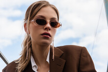 Young Woman In Sunglasses And Blazer Posing Against Blue Sky