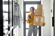 Young woman with parcels at the hallway at home, holds smart phone and checking goods. Concept of buying online and delivering goods home