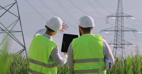 Wall Mural - engineers in white helmets looking at the poles of a high-voltage power line and point their hands a