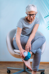 Wall Mural - Ankle Pain Treatment. Senior Woman Holding Ice Bag Compress on a Painful Ankle Joint.